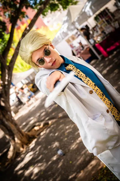 Cosplayer con peluca rubia y gafas redondas posando con una espada